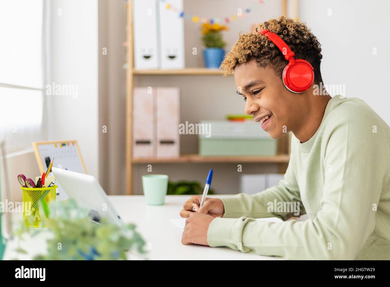 Sorridente giovane latino ispanico utilizzando il tavolo digitale per studiare online a casa Foto Stock