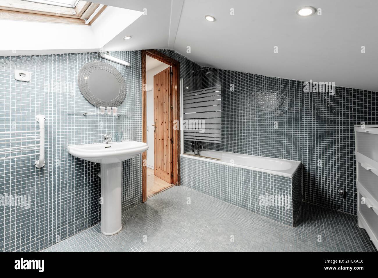 Grande toilette con soffitto inclinato piastrellato con piastrelle a mosaico sulle pareti e pavimento con toilette bianche Foto Stock