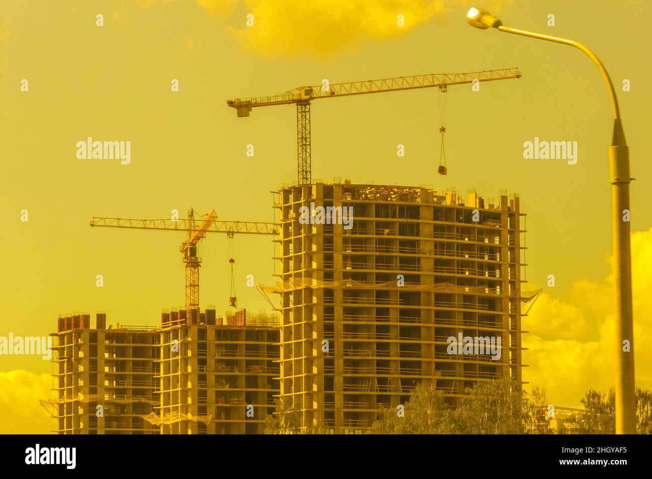 Costruzione industriale costruzione torre gru sullo sfondo di un cielo giallo soleggiato e lo sviluppo del tramonto. Foto Stock