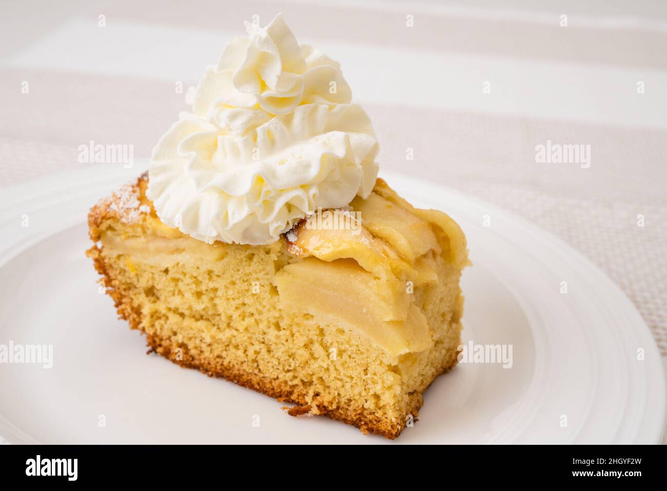 Fettine di torta di mele con base di biscotto e panna montata da vicino su un piatto bianco. Dolce di mele fatto in casa appena sfornato Foto Stock