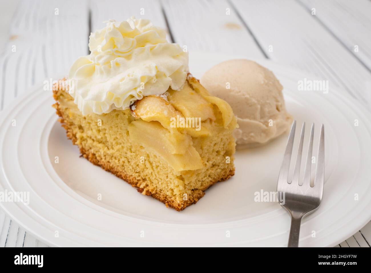 Pezzo di torta di mele con biscotto a base e panna montata, servito con gelato alla vaniglia da vicino su un piatto su sfondo bianco di legno Foto Stock