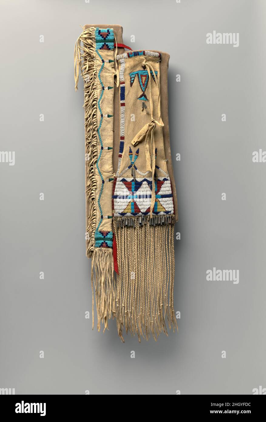 Sacco da tabacco con fusto ca. 1870 Northern Cheyenne, nativi americani la stretta manica di questa sacca di tabacco teneva il gambo di legno di un tubo. Una donna l’abbellì con piume stilizzate e una linea ondulata di adwork, forse per suggerire il ruolo del tubo nel trasmettere il fumo sacro e la preghiera. Un singolo Thunderbird, una potente spira, è rappresentato vicino all'apertura; motivi di clessidra, comuni nella pittura di Plains, trapuntature e disegni ricamati con perline, sono presenti sul corpo; e una frangia finemente ritorta a due veli pende dal basso. Sacco da tabacco con cassa tubo-gambo. Cheyenne settentrionale, America nativa Foto Stock