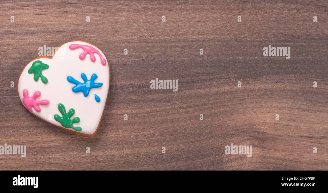 Biscotto colorato a forma di cuore glassato per San Valentino su sfondo di legno. Spruzzi di vernice. Spazio per il testo. Biscotto di Pasqua Foto Stock