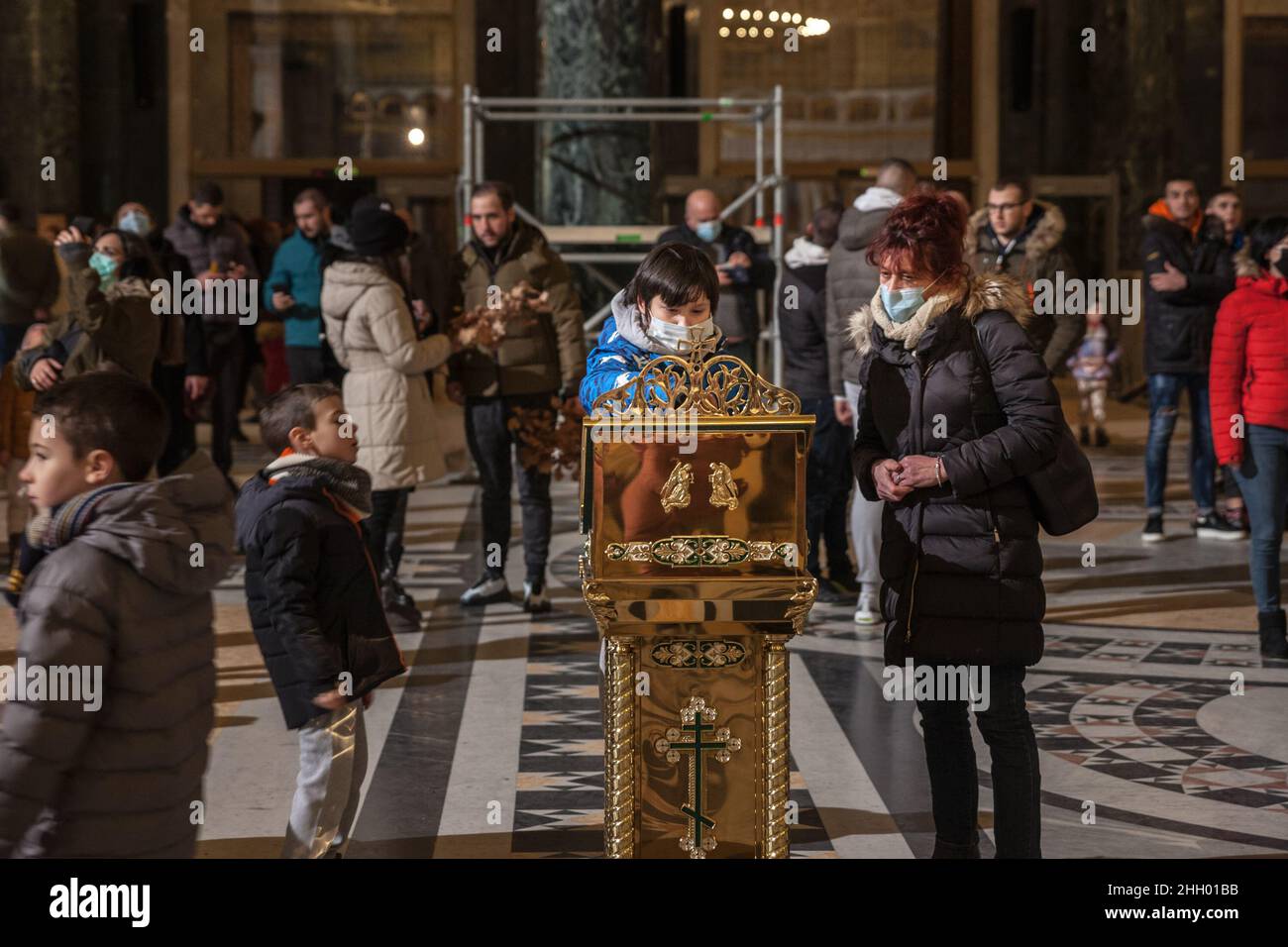 Foto di una famiglia bianca caucasica che prega indossando un facemask per la vigilia di Natale nella chiesa ortodossa del tempio di San Sava mentre indossava un protettore Foto Stock