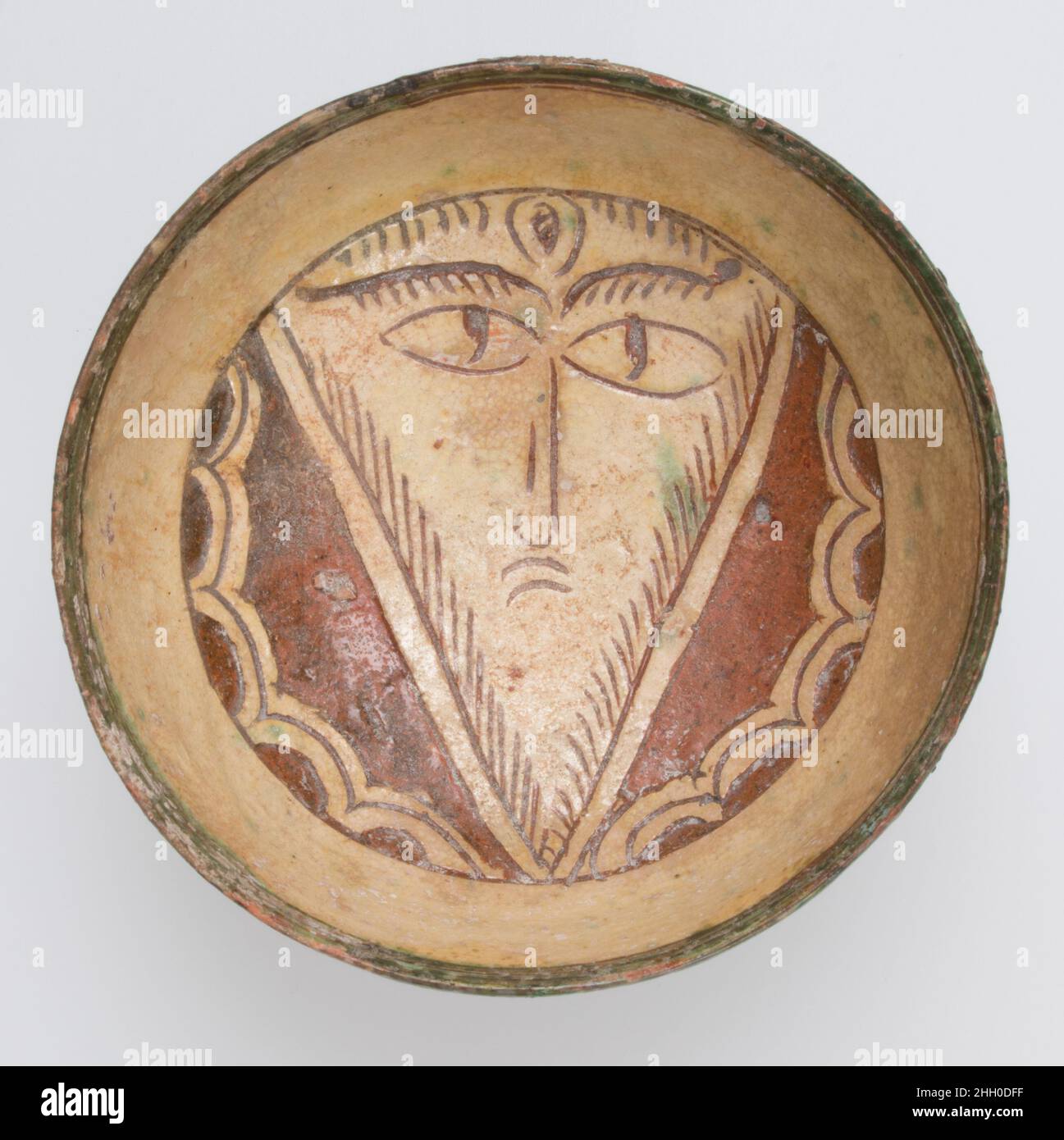 Ciotola con faccia 10th–13th secolo Bizantino la piccola ciotola di slipware, destinata all'uso domestico, mostra al suo interno il volto di un uomo inidentificato e barbuto. Il lavoro è tipico di slipware bizantino dove il corpo di argilla rossa di un vaso è stato coperto di slip (argilla liquida) che è stato poi tagliato, o incisa con linee, per creare un'immagine. Qui la barbottina è stata tagliata per formare il profilo della faccia triangolare con i suoi occhi fissanti, la barba e altri dettagli incisi nella barbottina rimanente. Ciotola con faccia. Bizantino. 10th–13th secolo. Terracotta, vetrata e sgraffito. Ceramica-ceramica Foto Stock