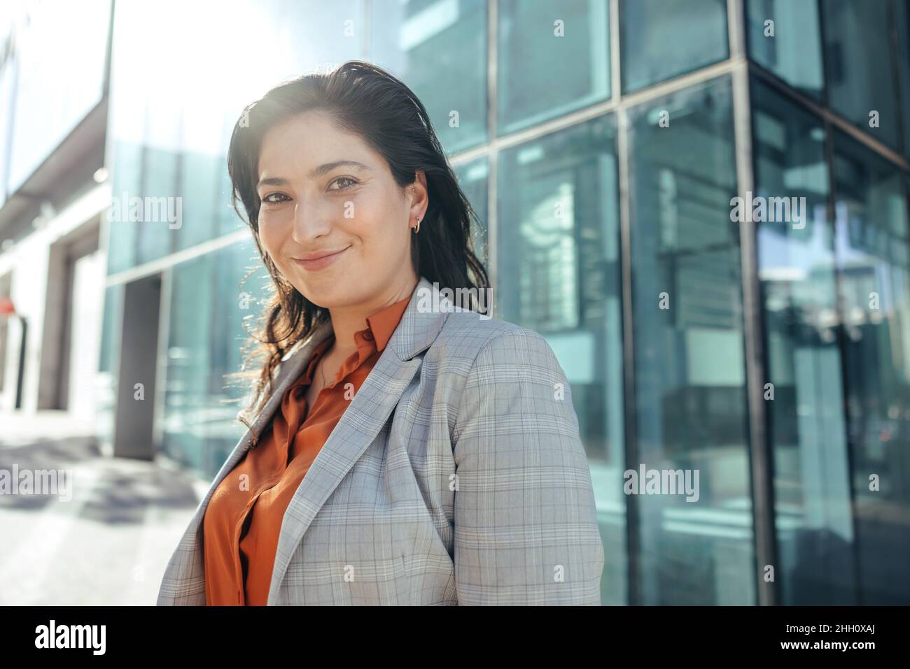 Felice donna d'affari sorridente alla macchina fotografica mentre si trova di fronte a un alto edificio di uffici in città. Imprenditore di successo femminile in piedi Foto Stock