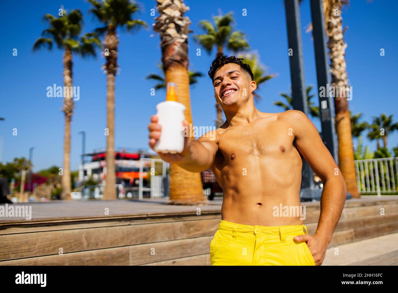 uomo latino che applica lozione di abbronzatura al mare con sfondo di palme Foto Stock