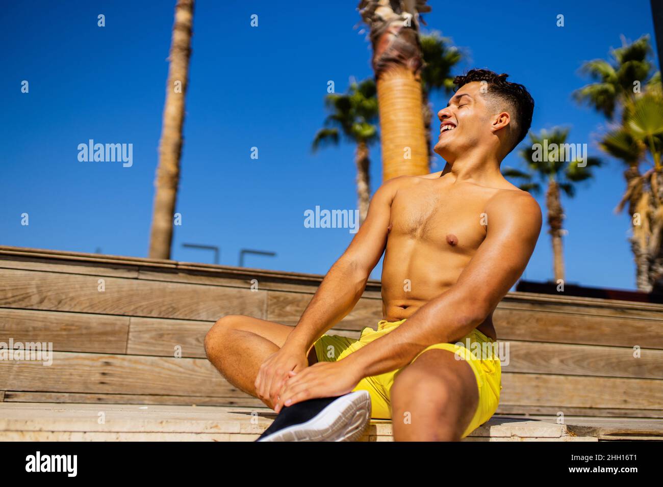 uomo latino che applica lozione di abbronzatura al mare con sfondo di palme Foto Stock