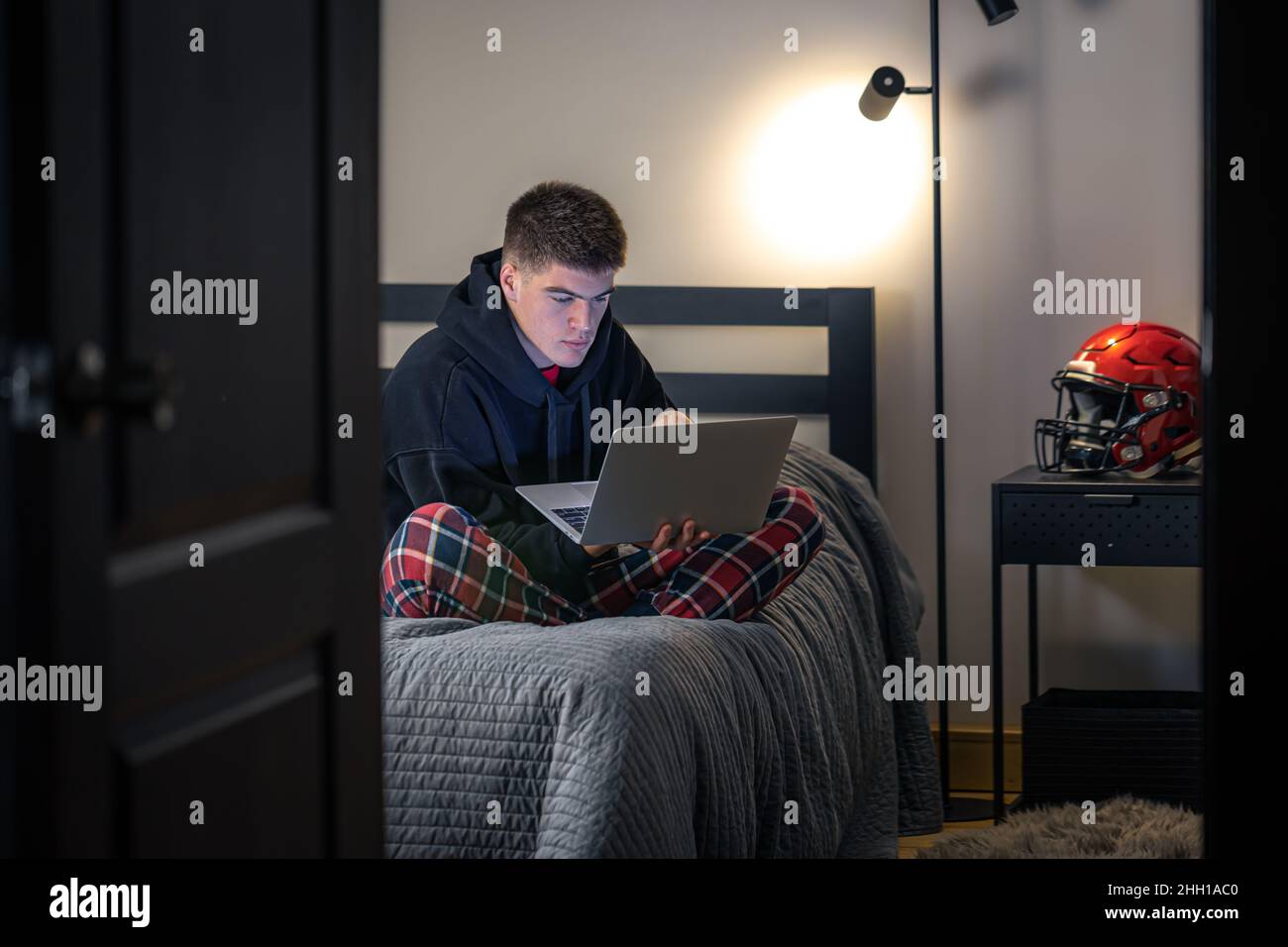 Un ragazzo si siede in una stanza su un letto e usa un computer portatile. Foto Stock