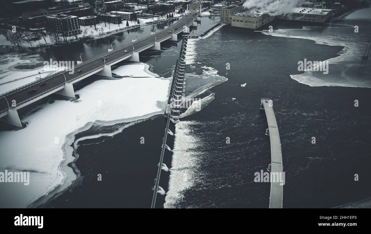 Panorama aereo su ghiacciato della città con tema desaturato per abbinare l'inverno freddo amaro. La diga scorre acqua nel fiume e traffico sul ponte Foto Stock