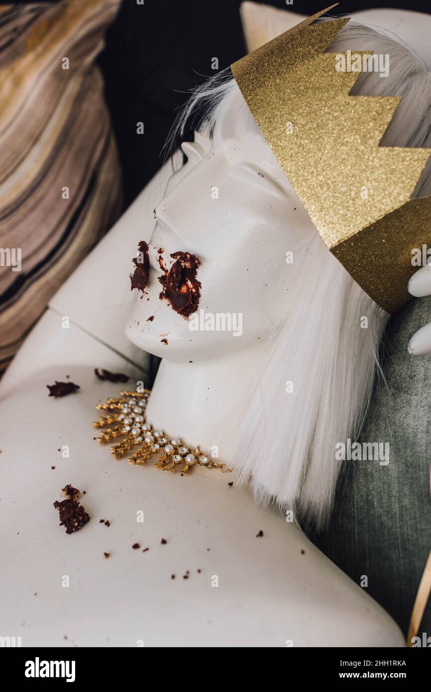 busto di manichino con corona d'oro e collana con torta al cioccolato spalmato sul viso Foto Stock