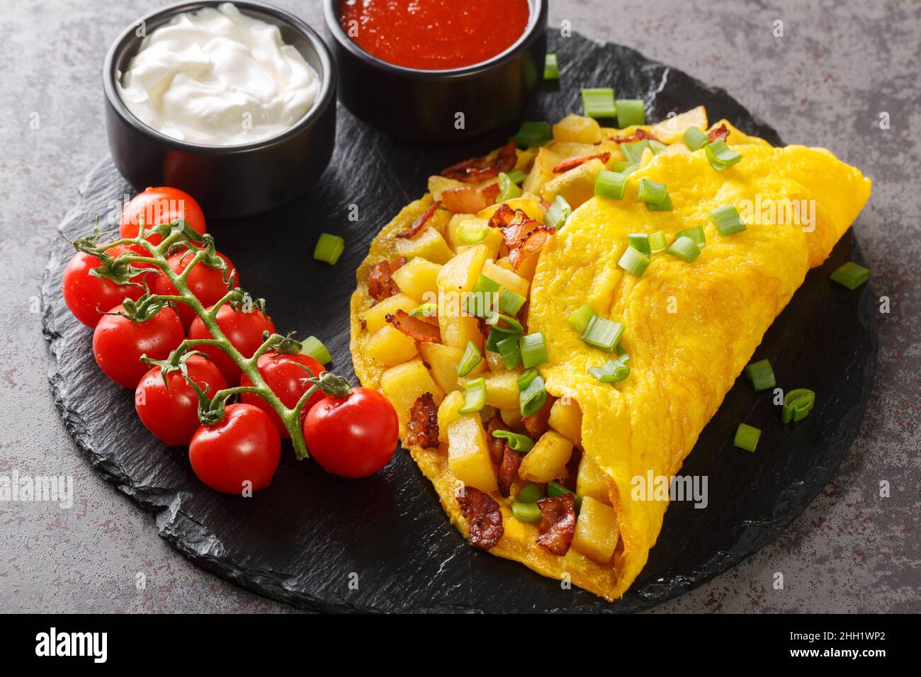 Deliziosa frittata contadina con patate fritte e pancetta da vicino su una tavola di ardesia su un tavolo di cemento. Orizzontale Foto Stock
