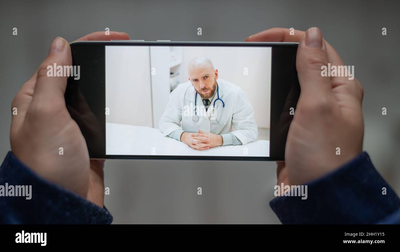 Medicina online. Il paziente parla con il medico tramite collegamento video mentre si trova a casa. Un uomo dà una consultazione medica remota su uno smartphone. Una donna è Foto Stock