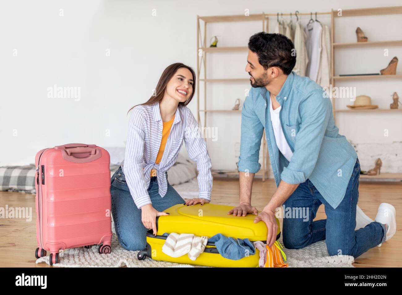 Sposi giovani amorevoli che si preparano per la vacanza, cercando di chiudere pieno di vestiti valigia, imballando le cose insieme Foto Stock