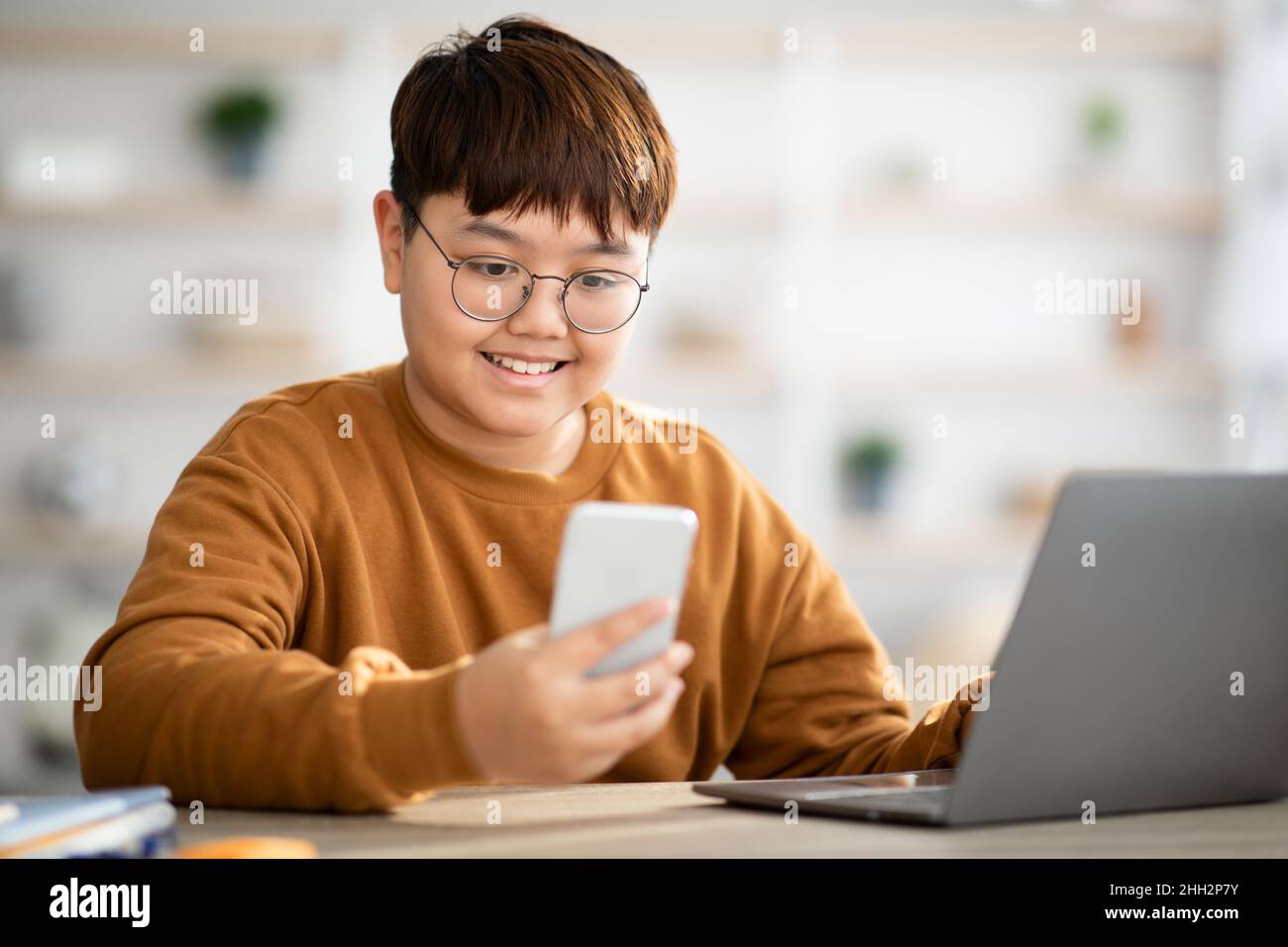 Il bambino asiatico positivo che usa il portatile e il telefono cellulare a casa Foto Stock