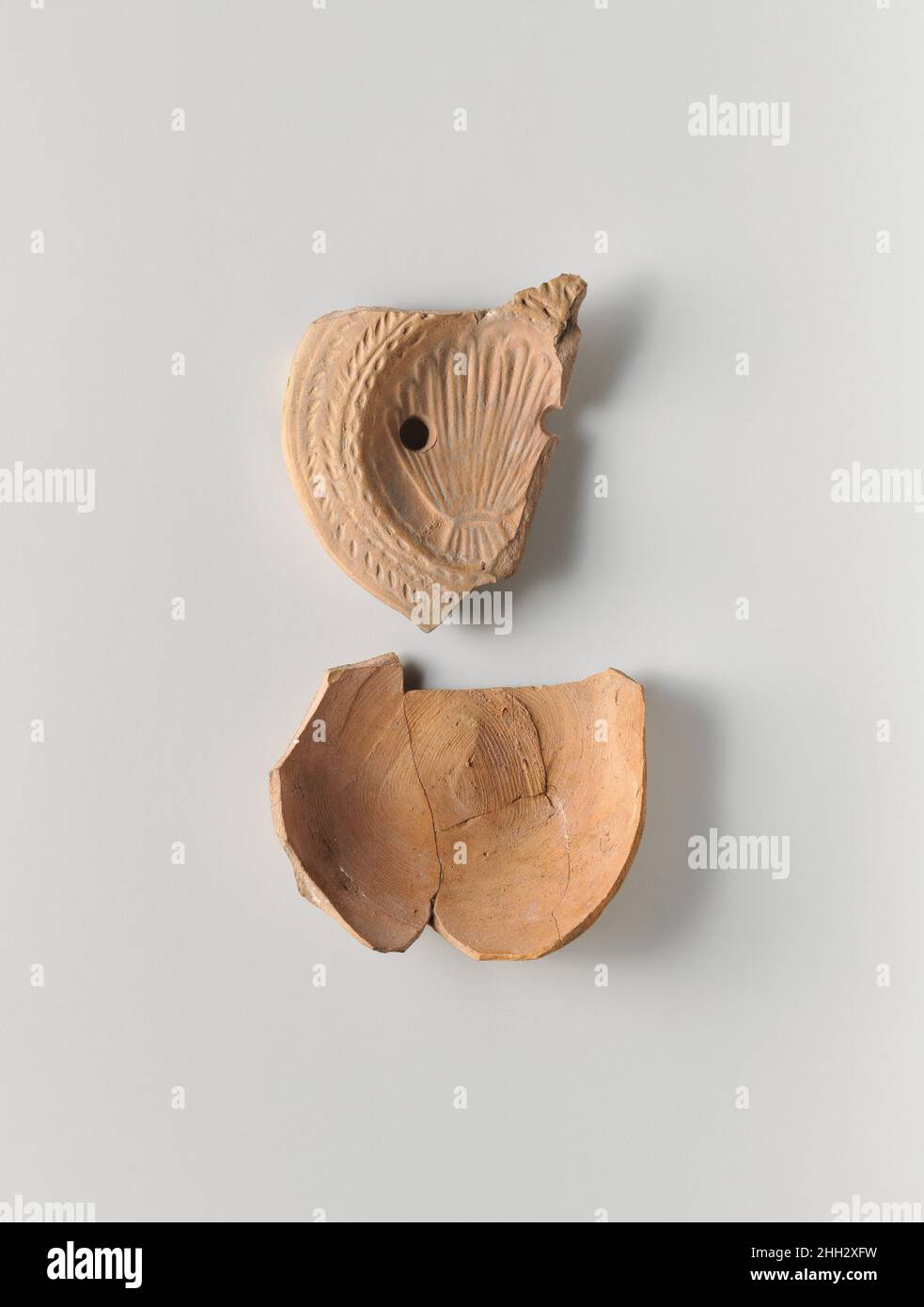 Lampada ad olio di terracotta ca. A.D. 200–350 Roman, Cypriot Loeschcke tipo 8. Realizzato in stampo. Discus: Conchiglia del cuoio capelluto; due fori di riempimento, uno per lato. Spalla, leggermente inclinata verso l'esterno: Banda stretta di punti impressi intorno al bordo del disco e ampio disegno a spina di pesce impresso. Base concava indefinita; sulla base, scritta in grandi lettere greche in tre righe: C?YPI?WNOC, 'di Sphyridon.' rotta e riparata, ora in due pezzi separati, comprendente parte di disco e spalla come pezzo unico, e in quattro pezzi Uniti parte di lato e la maggior parte di base. Argilla di buccia rossastra.. Lampada ad olio di terracotta. Romana, Foto Stock