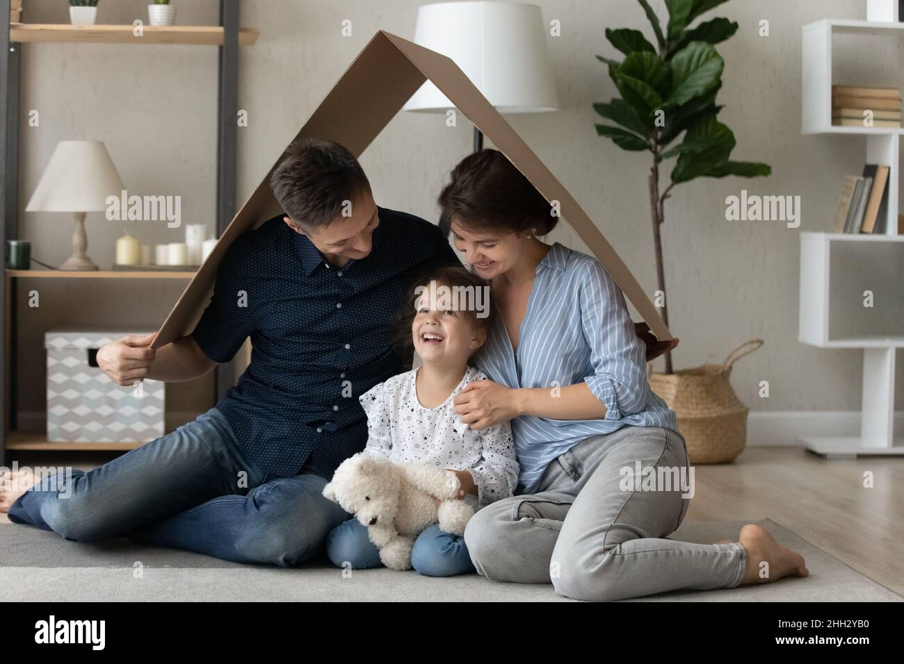 Felice legame con i giovani genitori seduti sotto il tetto di cartone con la figlia. Foto Stock