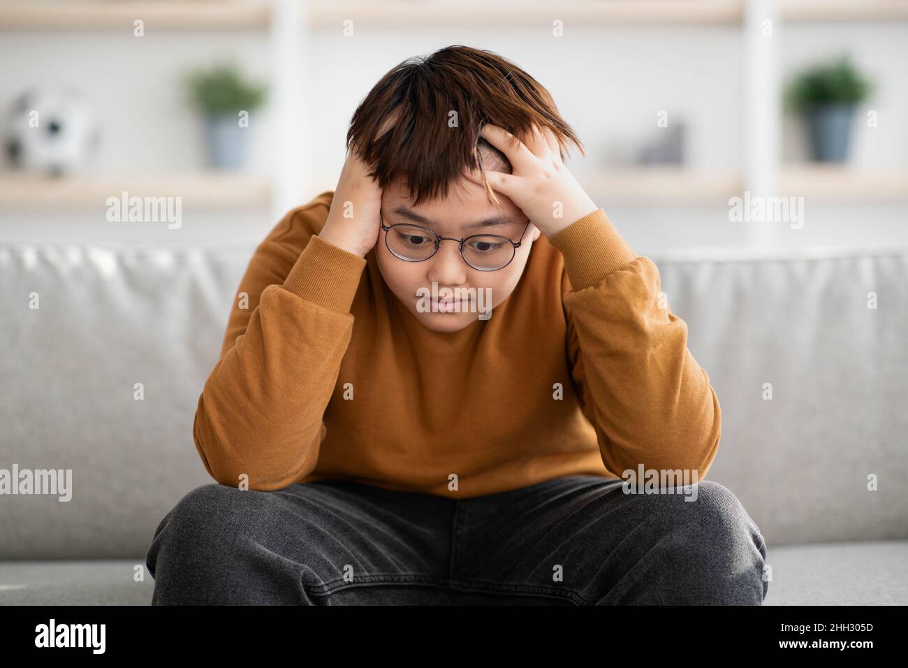 Ragazzo asiatico frustrato che tocca la testa, interno a casa Foto Stock