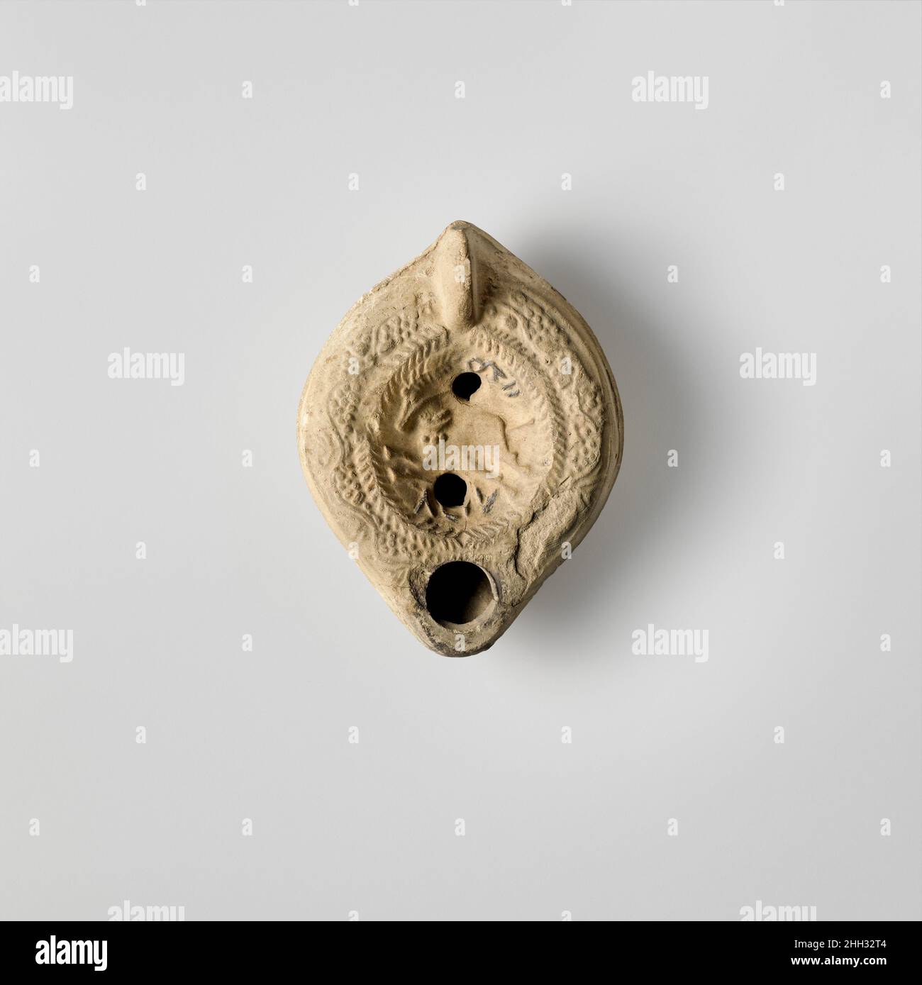 Lampada ad olio di terracotta 4th–5th secolo d.C. romana, cipriota Vessberg tipo 18. Impugnatura non forata. Realizzato in stampo. Discus: Cavallo da corsa vittorioso a sinistra e con colletto ornato, con ramo di palma sopra la testa, fiancheggiato da entrambi i lati da corona di herringbone. Sopra il cavallo: Lettere indistinte; sotto il cavallo: Lettere indistinte. Due grandi fori di riempimento sopra e sotto il cavallo. A spalla, tendine di vite con grappoli di uva stilizzati. Su base indefinita, leggermente concava, in rilievo, lettere greche: EYTYXHTOC.intatto, tranne per leggere perdite superficiali a destra. Fuliggine intorno all'ugello. Argilla di buccia pallida.. Olio di terracotta lam Foto Stock