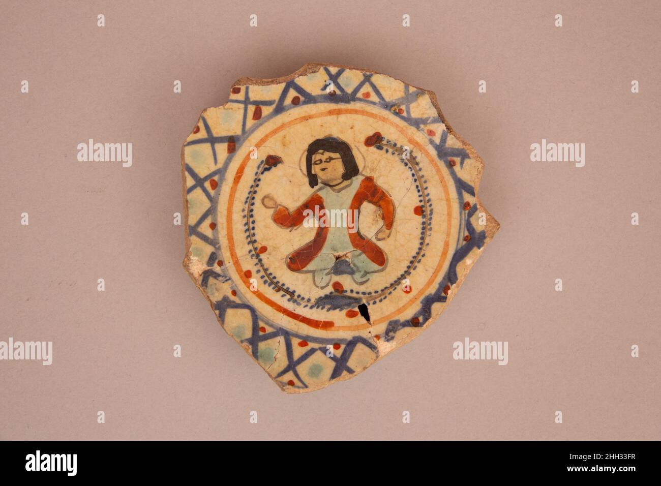 Frammento di un vaso Mina'i del 13th–12th secolo questo frammento è dipinto con una figura seduta circondata da rami punteggiati racchiusi in un medaglione. La tecnica pittorica, ora chiamata mina'i ma storicamente chiamata haft rang (sette colori), era una tradizione iraniana distintiva impiegata sulla stonepaste, possibilmente trasposta dalla smaltatura del vetro. I prodotti dipinti di Mina'i condividono alcune caratteristiche stilistiche con la stonepasta siriana coeval, tra cui i volti lunari delle figure o i rami punteggiati visti su questo pezzo, che esemplificano come un comune linguaggio visivo sia stato adattato e modificato da loc Foto Stock