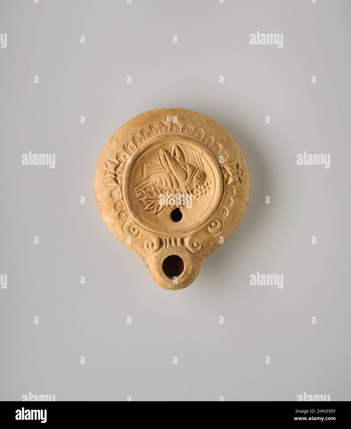 Lampada ad olio di terracotta ca. A.D. 90–200 Loeschcke romano tipo 8. Modellare, con corpo poco profondo e profondamente carinato. Discus: Locusta di fronte a destra, mangiare l'uva; un unico foro di riempimento in basso. Sulla spalla, un disegno di ovuli impressi, interrotti ai lati con due disegni a forma di testa d'ascia. Palette stilizzate con ugello di fiancheggiamento. Anello di base delineato da due scanalature concentriche, e una base piatta, con un segno impresso del marcatore, comprendente due lettere greche: C ?, fiancheggiando uno spray con tre bacche. Clay.intact.The lampada è stato probabilmente fatto in Siria–Palestina.. Lampada ad olio di terracotta. Romana. CA. D. Foto Stock