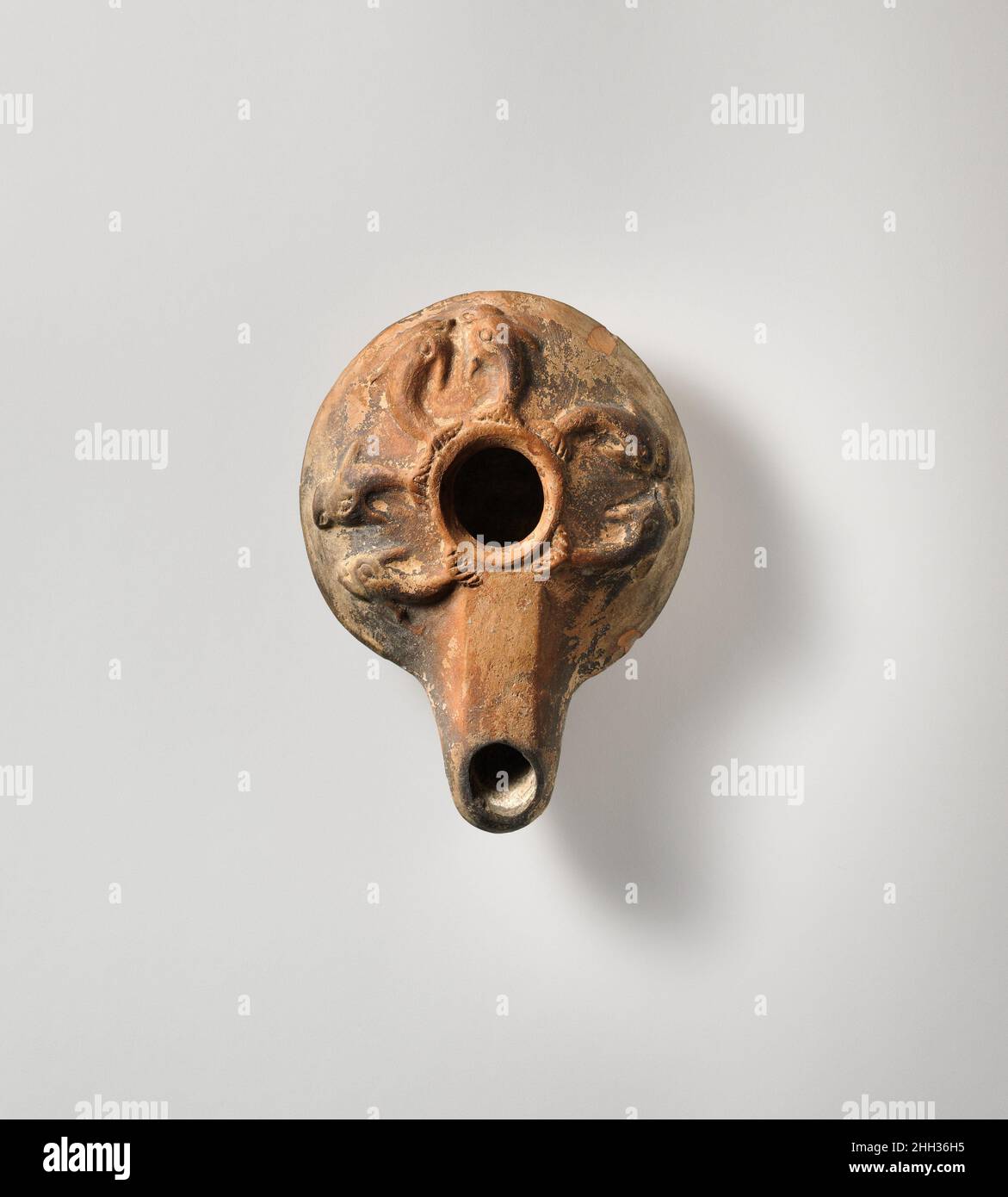 Lampada ad olio di terracotta metà 2nd–1st secolo a.C. greco Mold-made. Corpo poco profondo e carinato con ugello lungo. Grande foro centrale di riempimento; ampia spalla inclinata decorata con tre paia di delfini, rivolti verso l'esterno e verso il basso. Base rialzata, piatta, scritta in greco: ???coi. Intatto... Lampada ad olio di terracotta. Greco. Metà 2nd–1st secolo a.C. Terracotta; modellata. Ellenistico. Terracotte Foto Stock