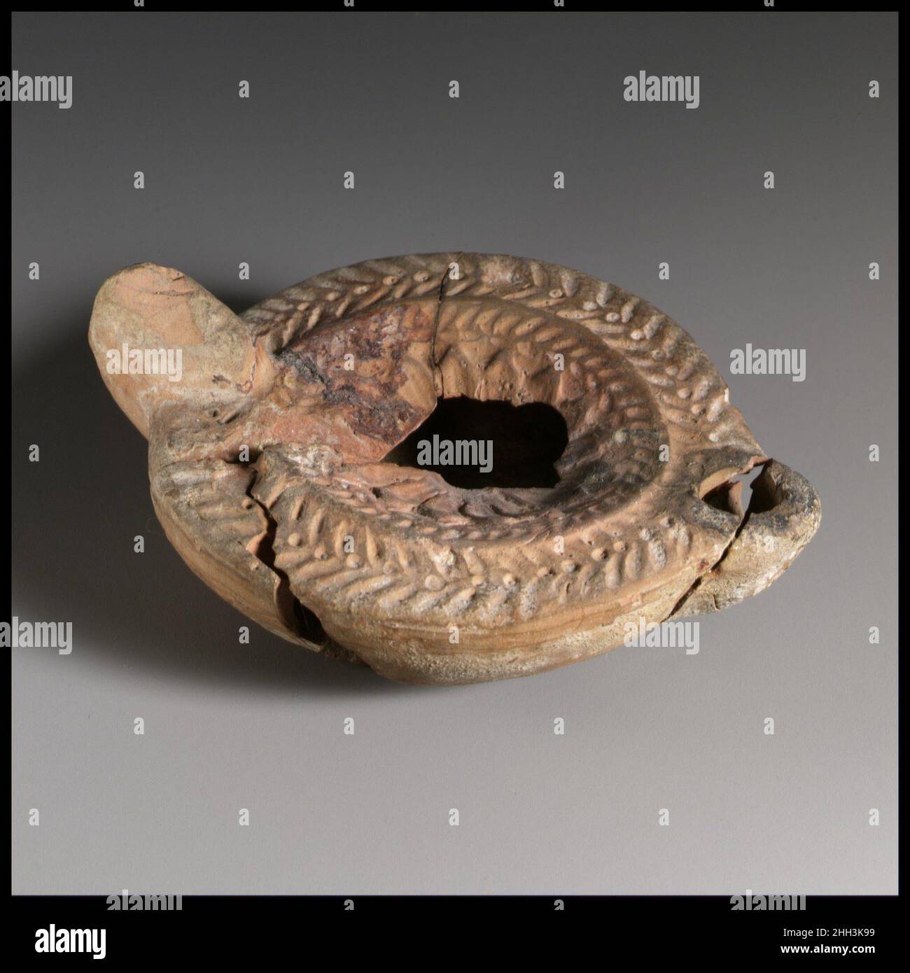 Lampada ad olio in terracotta 1st metà del 3rd secolo d.C. Loeschcke romano tipo 8. Impugnatura non forata. Realizzato in stampo. Discus: Rosetta circondata da una corona di aringhe impressa. Sulla spalla: Corona d'aringa. Sulla base, in lettere greche: ?PMIA/[N]O.. Lampada ad olio di terracotta. Romana. 1st metà del 3rd secolo d.C.. Terracotta, modellata. Tardo imperiale. Terracotte Foto Stock