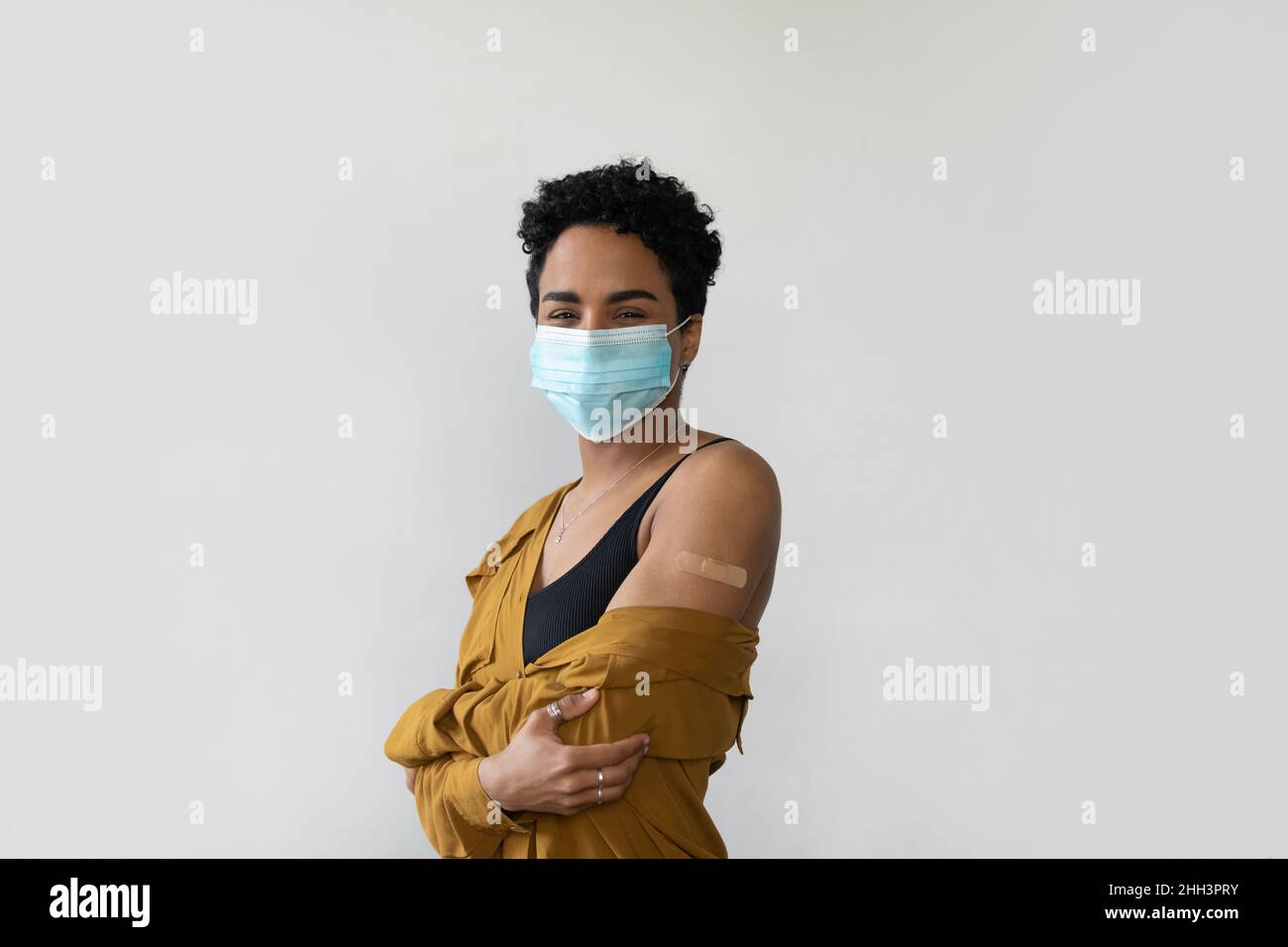 Felice donna africana millenaria in faccia maschera medica mostrando braccio Foto Stock