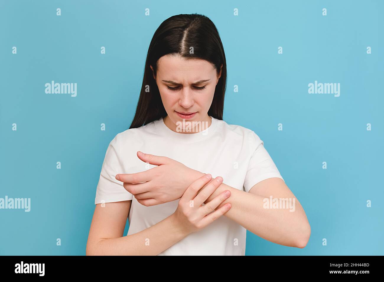 Ritratto di stanco giovane donna braccia che tiene il suo polso doloroso causato da un lavoro prolungato, isolato su sfondo blu. Sindrome del tunnel carpale, artrite Foto Stock