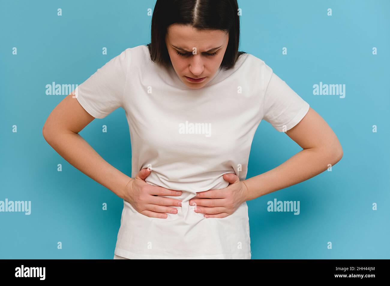 Triste giovane donna che sperimenta dolore di stomaco, isolato sulla parete di fondo blu studio. Donna millenaria affetta da mal di stomaco, affetta da seve Foto Stock