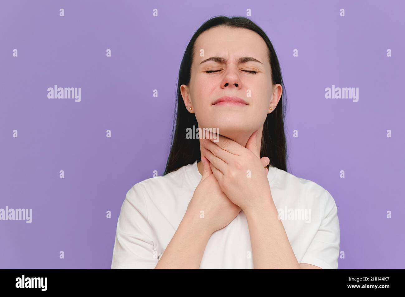 Primo piano di una giovane donna malata affetta da mal di gola, isolata sulla parete viola dello studio. Le cause del dolore della gola includono influenza, raffreddore comune, batterico in Foto Stock