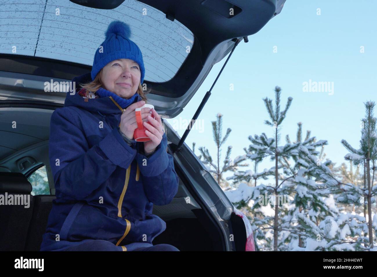 Sciatore maturo che ha il tè mentre si siede sul retro del suv dopo il sentiero della foresta di wintry. Attività all'aperto per aumentare l'umore durante la pandemia di coronavirus in inverno Foto Stock
