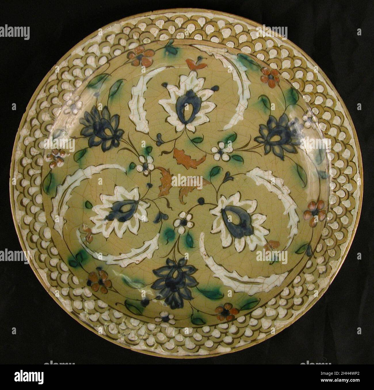 Piatto con disegni floreali su sfondo olivo 16th–17th secolo questo piatto fa parte di un gruppo di ceramiche conosciute come Kubachi ware. Chiamato per un villaggio nel Caucaso in cui questa ceramica è stata scoperta in quantità, i prodotti Kubachi sono ora si pensa che siano stati effettivamente prodotti a Tabriz. Un'applicazione irregolare dello smalto ha portato ad un crepitio a superficie larga, caratteristica tipica dei prodotti Kubachi. Questo piatto mostra un debito distinto alla ceramica Iznik dimostrato nei colori utilizzati, il disegno in scala di pesce sul bordo, e soprattutto le forme vegetali di melograno e foglia di saz nel centr Foto Stock