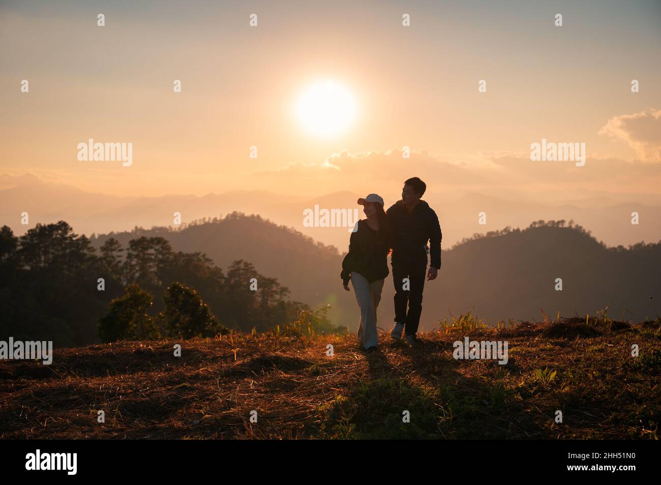 Silhouette giovane coppia asiatica abbracciando godendo in collina in campagna al tramonto Foto Stock