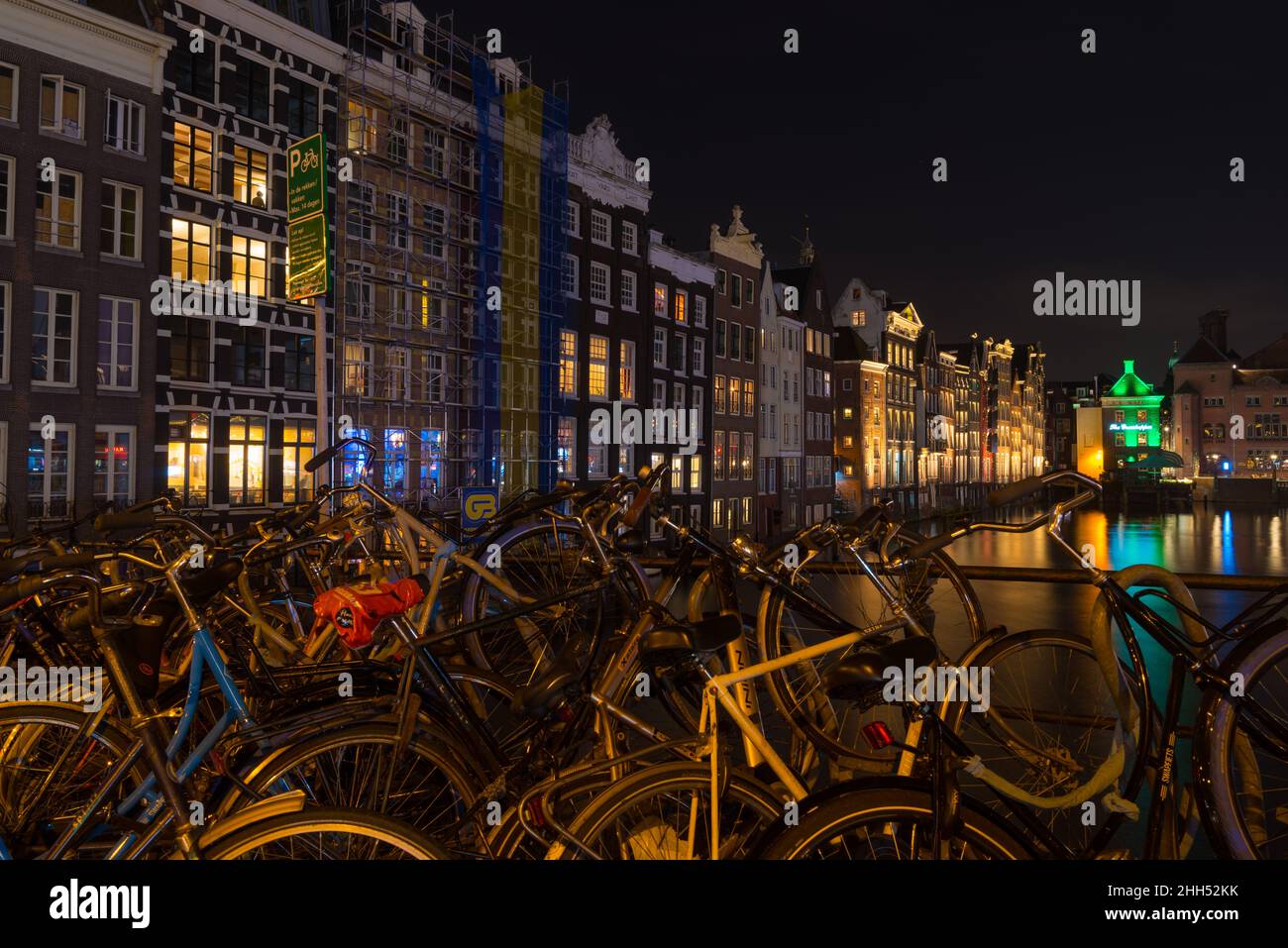 AMSTERDAM - 14 DICEMBRE 2019: Le famose case dei canali danzanti sul canale Damrak di notte con un sacco di biciclette nella parte anteriore Foto Stock