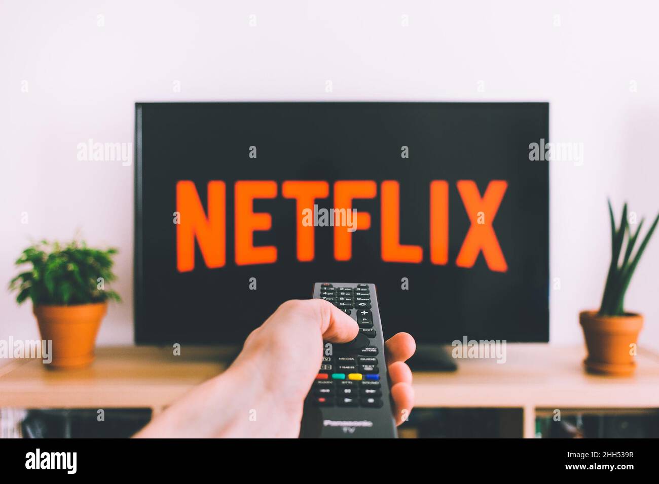 Uomo che guarda Netflix su un televisore nero su uno sfondo bianco mentre  tiene un telecomando con tasti colorati Foto stock - Alamy