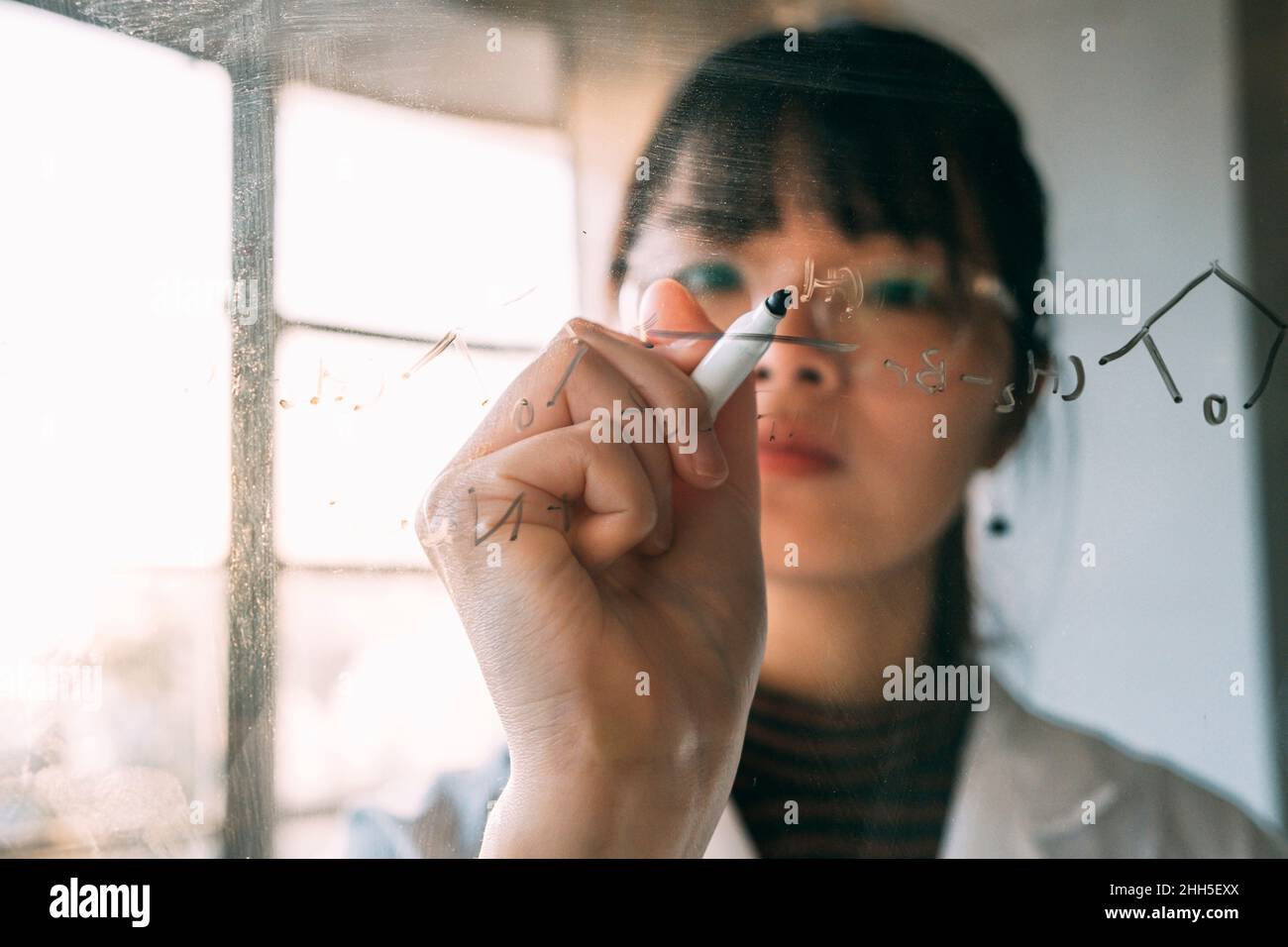 Giovane scienziato che scrive su vetro trasparente in laboratorio Foto Stock