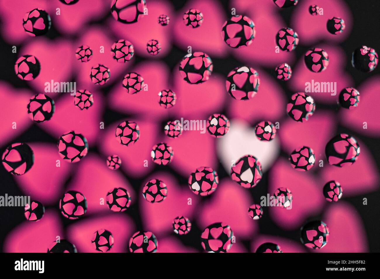 Cuori rosa e bianco su sfondo nero dietro il vetro con gocce di pioggia Foto Stock