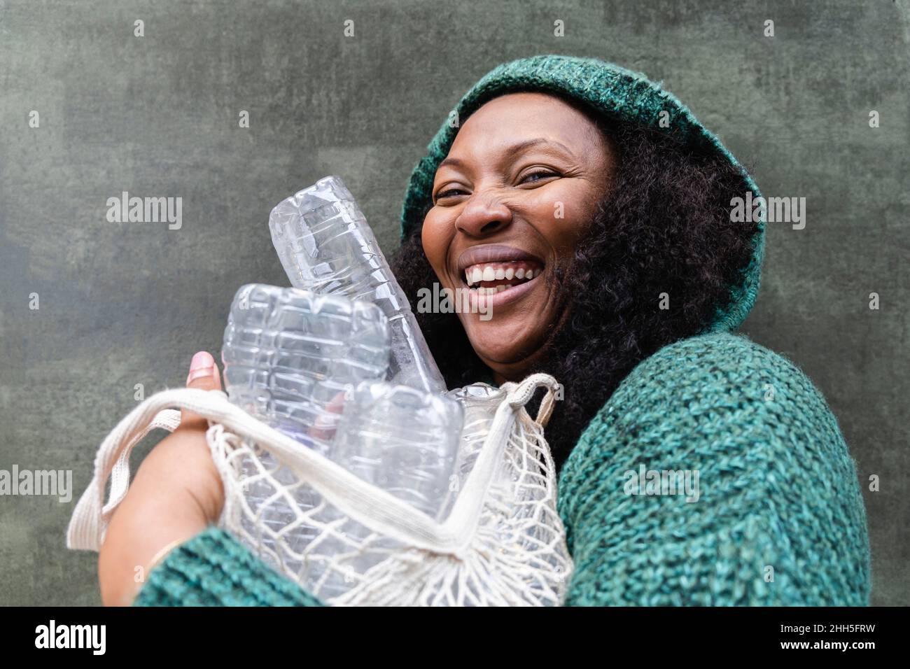 Donna felice che tiene bottiglie d'acqua di plastica in sacchetto di rete Foto Stock