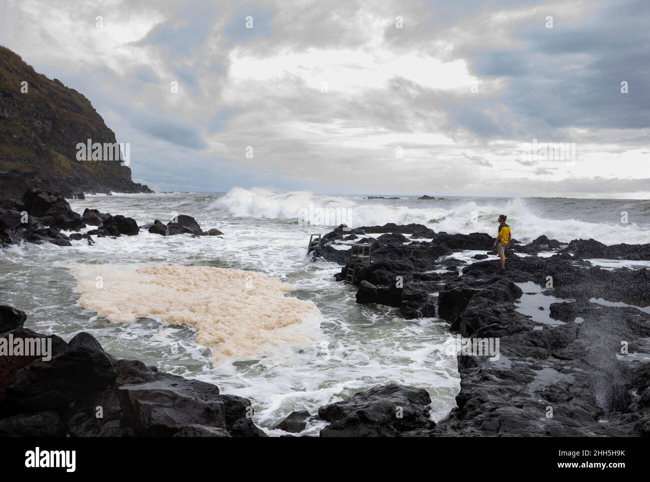 Uomo in piedi su rocce vicino alla piscina termale a Ponta da Ferraria, San Miguel, Azzorre, Portogallo Foto Stock