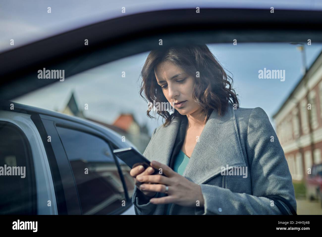 Donna che usa il telefono cellulare alla porta dell'auto aperta Foto Stock
