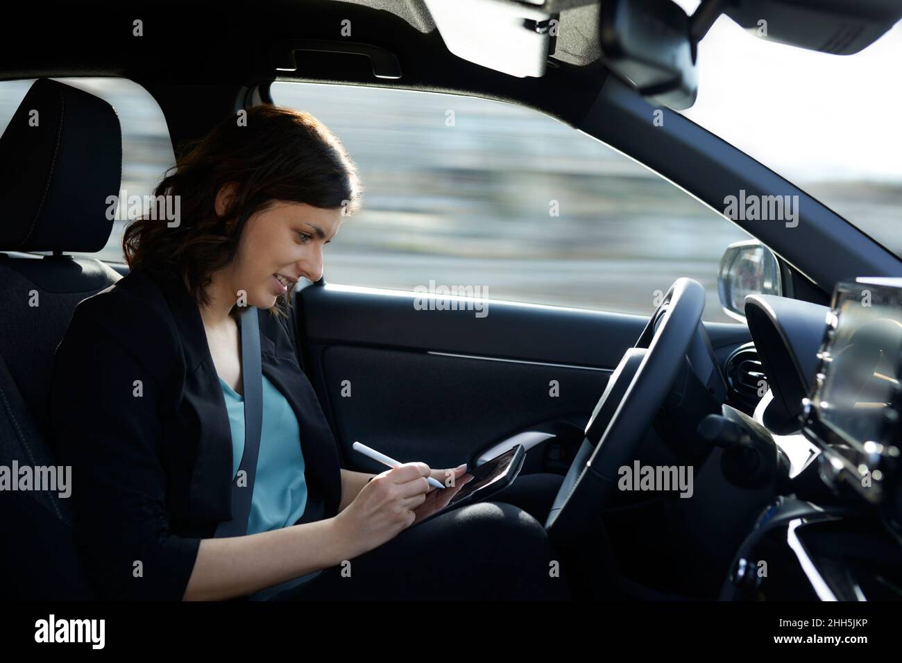 Donna d'affari sorridente che usa un tablet PC in un'auto a guida autonoma Foto Stock