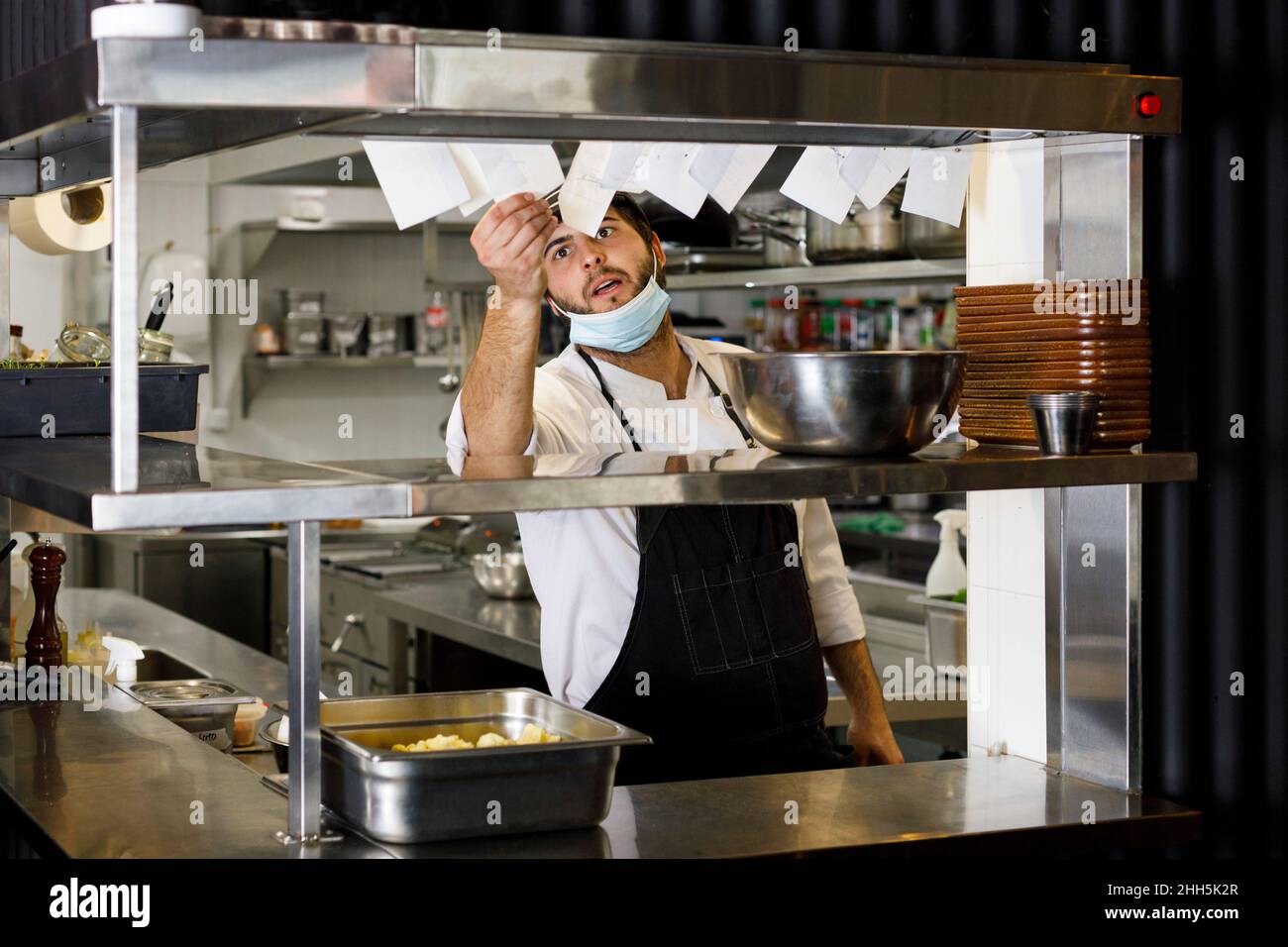 Chef con maschera protettiva controlla il titolare del biglietto nel ristorante Foto Stock