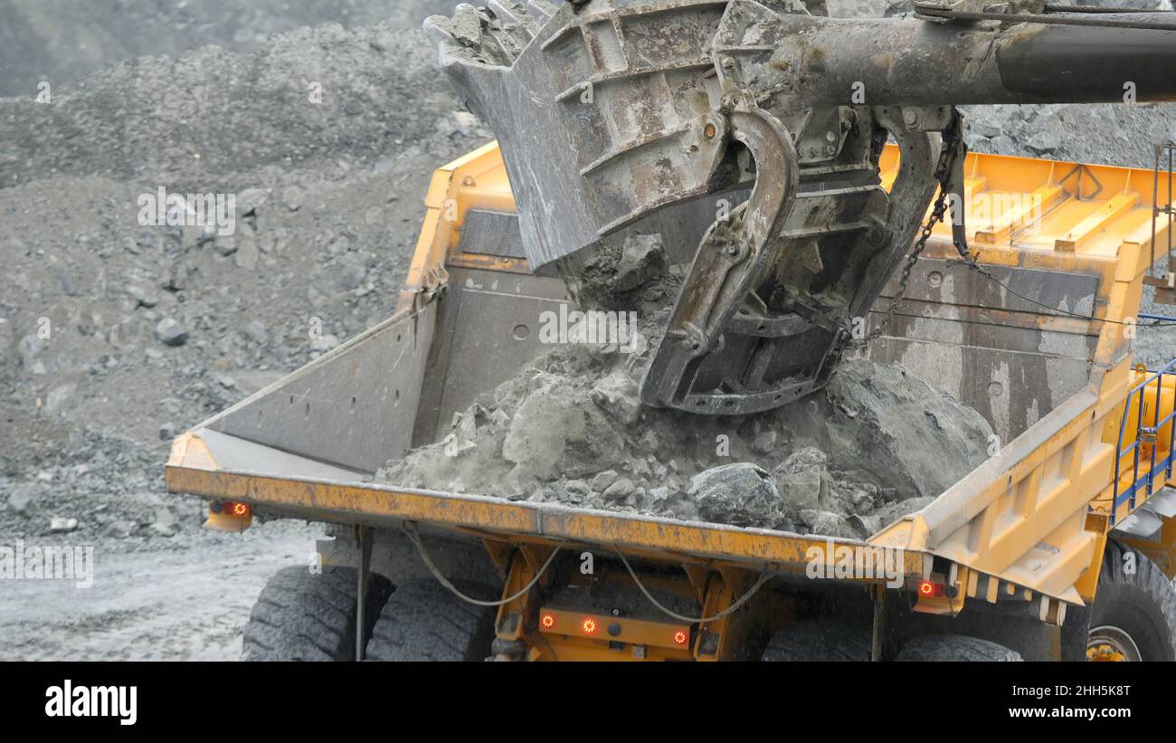 Primo piano dell'escavatore che carica il dumper con il minerale nella cava. Industria mineraria Foto Stock