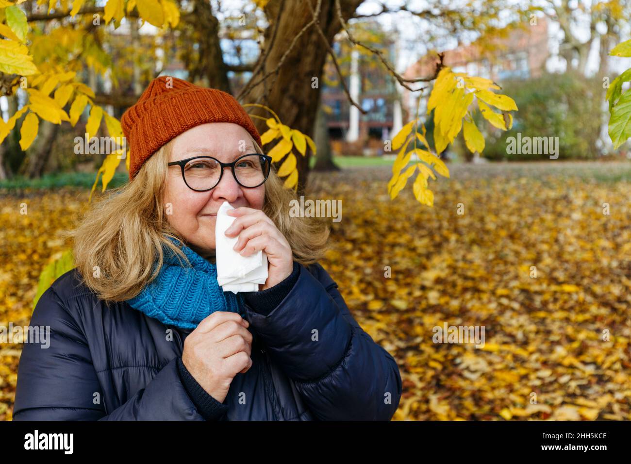 Donna anziana che soffia il naso con carta tissue nel parco autunnale Foto Stock