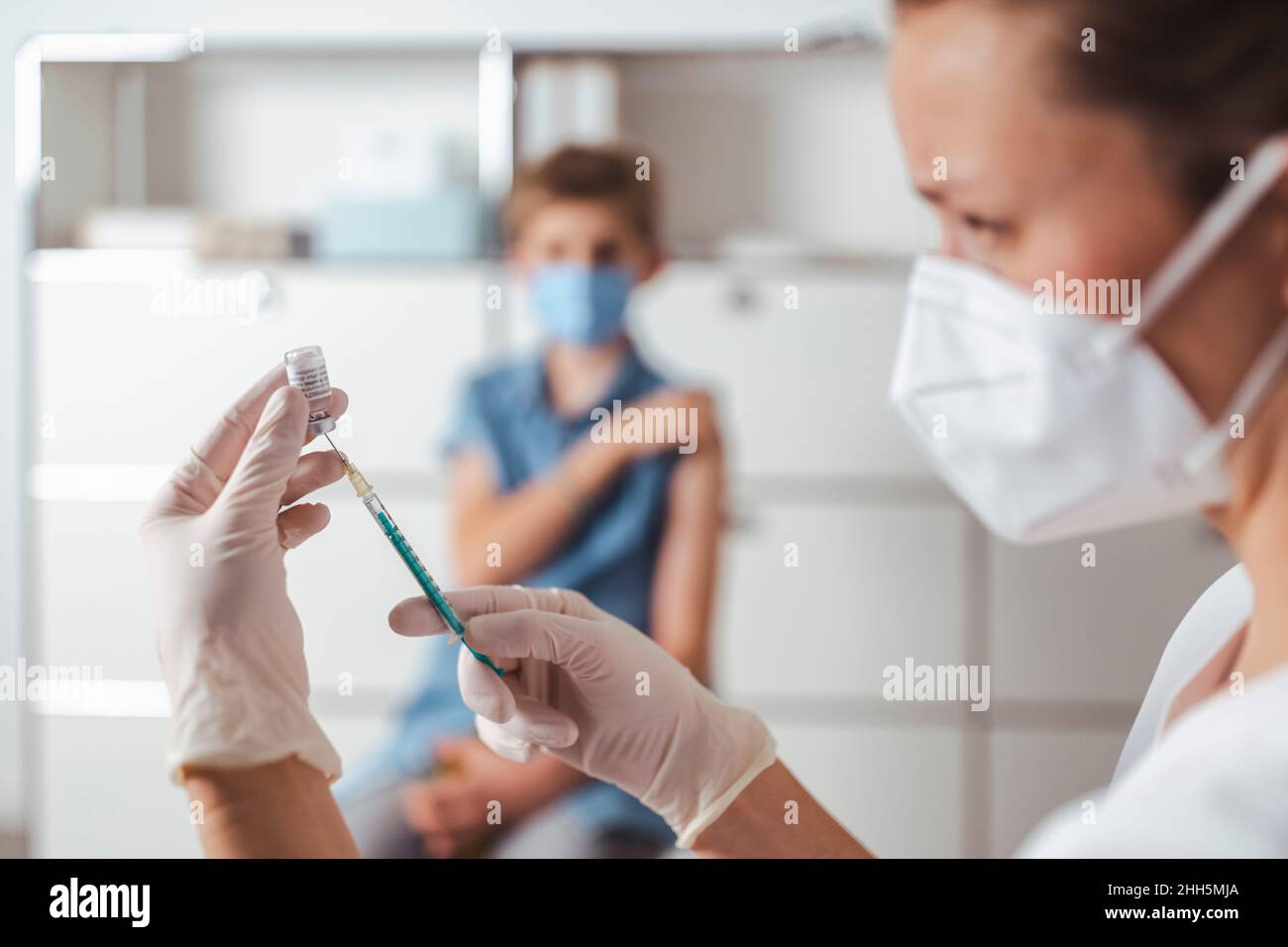 Infermiere che prepara il vaccino COVID-19 con il ragazzo in background al centro Foto Stock