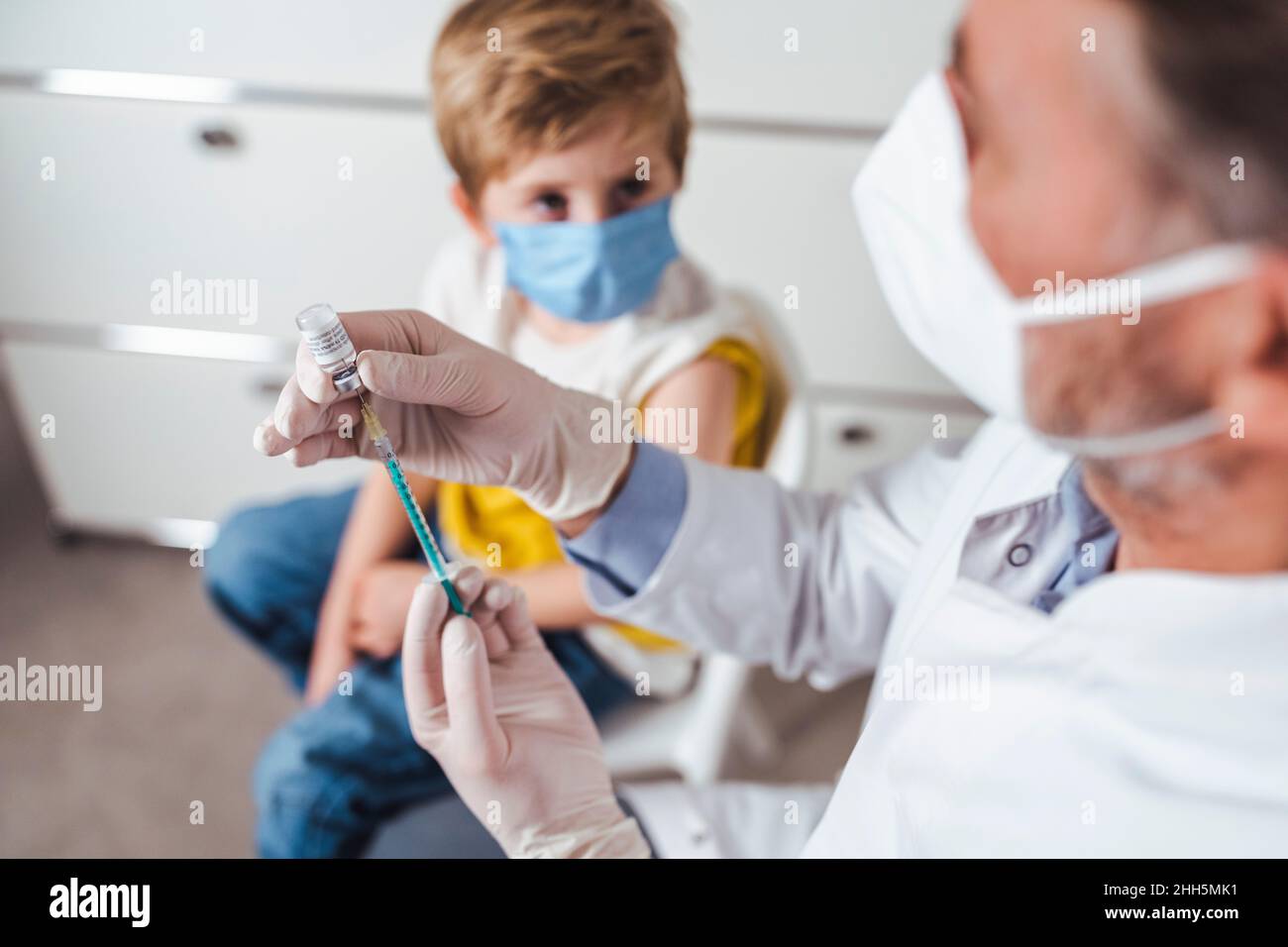 Medico che prepara l'iniezione di vaccino per il ragazzo in background al centro Foto Stock