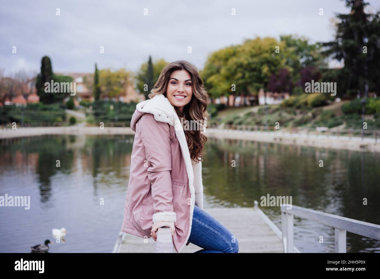 Donna sorridente seduta sulla ringhiera del molo Foto Stock