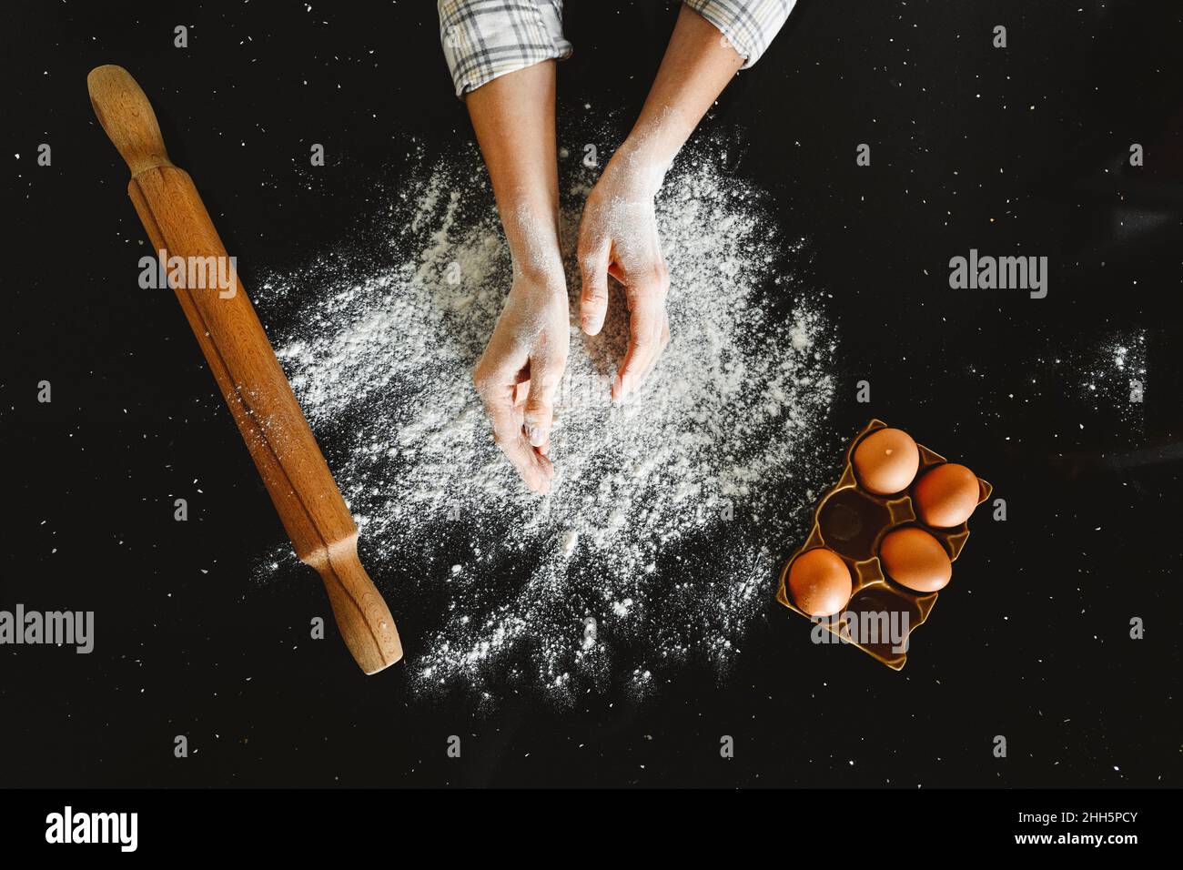 Donna che spolvera la farina dal vassoio delle uova su sfondo nero Foto Stock