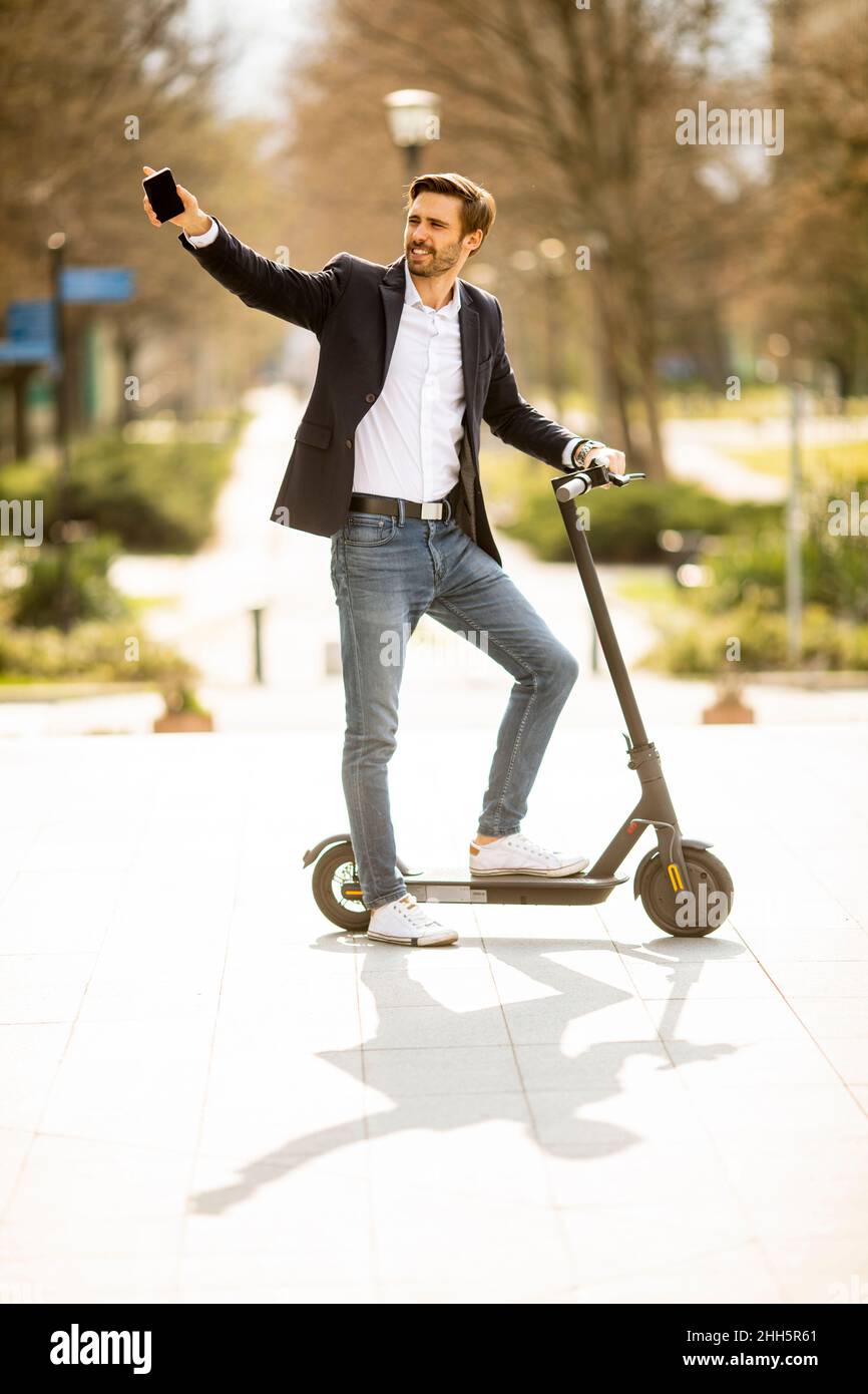 Bel giovane uomo d'affari che usa il telefono cellulare su scooter elettrico Foto Stock